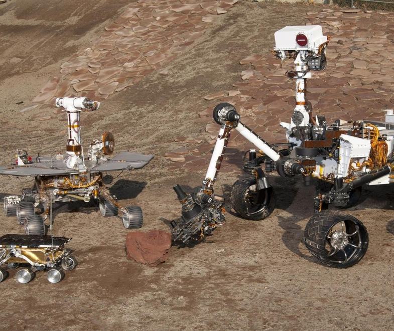 Three Mars rover designs positioned together on a rocky test terrain.