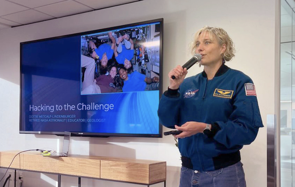 Retired NASA astronaut Dorothy Metcalf-Lindenburger wearing blue NASA jacket and speaking into a microphone
